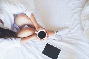 Relaxing young woman enjoying her coffee while sitting in bed.