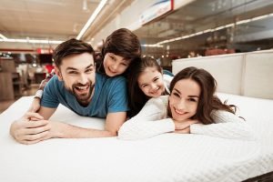 Young Happy Family Relaxing on Soft Bed in Store