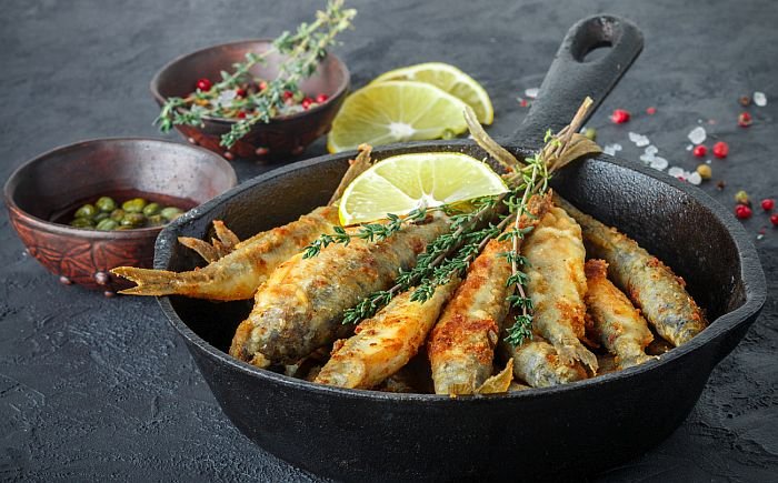 Fried smelt in a frying pan on the table with lemon, thyme, capers, spices and red onion. Small fish