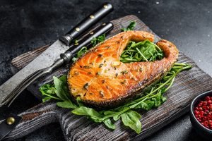 Baked salmon steak with arugula and pepper. Black background. Top view