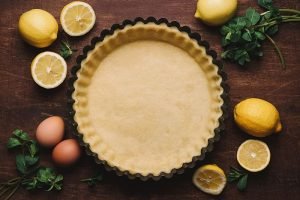 Circular metal flan tin lined with shortcrust pastry. Ingredients for making lemon tart. Home baking concept