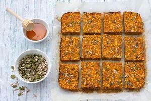 Carrot bars with oatmeal, dried apricots, seeds and honey on a light blue background
