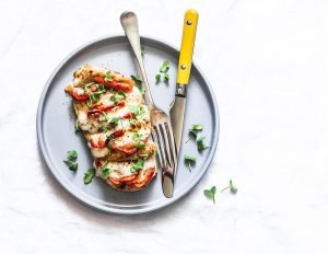 Baked chicken fillet stuffed with tomatoes and mozzarella on a light background, top view
