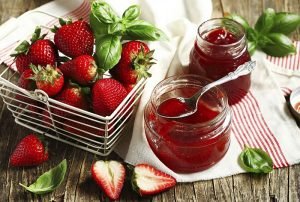 Homemade delicious strawberry jam with basil in a glass jar and fresh strawberries on table