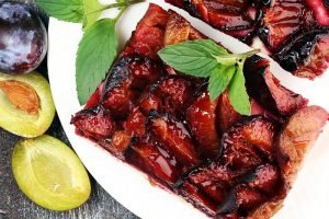 Rustic plum cake on wooden background with plums around.