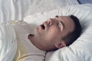 Portrait of a man sleeping with an open mouth. problem of snoring during sleep. A young cute guy sleeps on a white bed at day or morning
